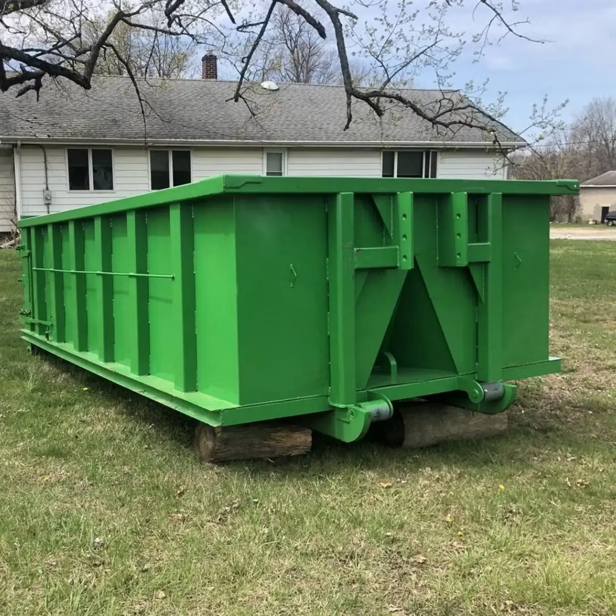 Green roll-off dumpster on boards in front of a house